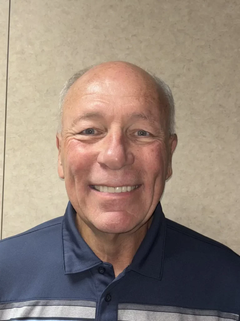 Smiling older man wearing a navy polo shirt indoors.