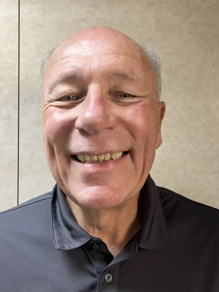Smiling older man wearing a navy polo shirt indoors.
